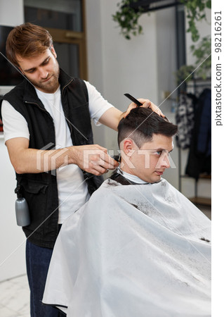 Barber shaving caucasian man in barber shop. 98216261