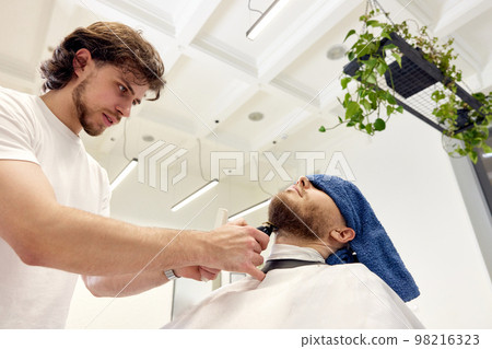Barber shaving bearded man in barber shop. Barber shaving bearded man in barber shop. 98216323