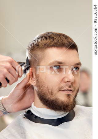 Barber trim hair with clipper on handsome bearded man Barber trim hair with clipper on handsome bearded man 98216364