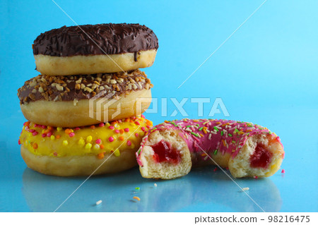 Yellow pink chocolate donuts lie a stack of a row of cut-off bitten doughnut stuffed with pink chocolate on a blue bright background with room for text. still life from food 98216475