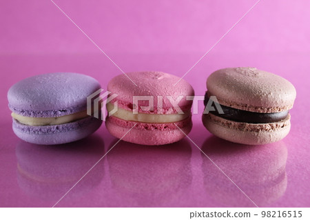 Three macaroons lilac brown chocolate lavender pink lie in a row on a pink fuchsia-colored background with reflection and a place for text and copyspace 98216515