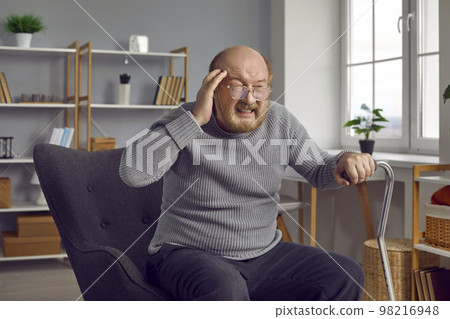 Stressed retired senior citizen with a migraine is sitting in his armchair at home Stressed retired senior citizen with a migraine is sitting in his armchair at home 98216948