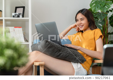 Cheerful young woman wear orange shirt with sitting on sofa and using laptop computer at home. 98217061
