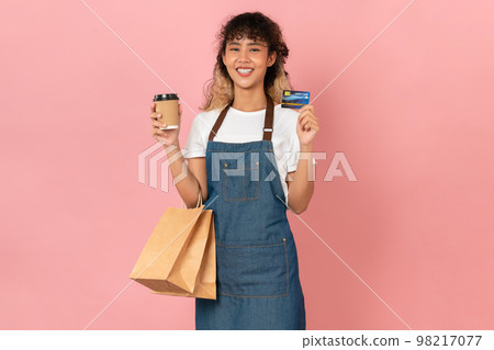 Asian woman wears an apron and holding brown blank paper shopping bags and showing credit card Asian woman wears an apron and holding brown blank paper shopping bags and showing credit card 98217077