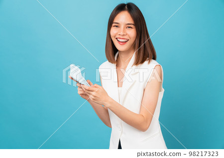 Cheerful beautiful Asian woman stand with hand holding white calculator on blue background. Cheerful beautiful Asian woman stand with hand holding white calculator on blue background. 98217323
