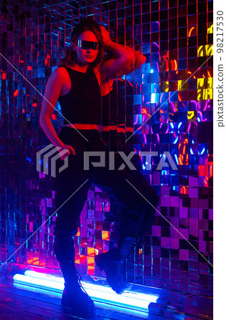 Portrait of a caucasian woman in sunglasses in neon light against a mirror wall. Portrait of a caucasian woman in sunglasses in neon light against a mirror wall. 98217530