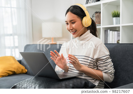 Asian woman wearing headphones and look to laptop at video calling meeting and study online Asian woman wearing headphones and look to laptop at video calling meeting and study online 98217607