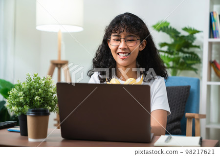 Young cheerful woman sitting on sofa and using laptop computer at home. 98217621
