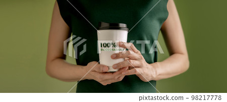 Biodegradable and Compostable Packaging Concept. Closeup of Woman Holding a Hot Cup of Coffee against a Green Wall. Zero Waste Materials. Environment Care, Reuse, Renewable for Sustainable Lifestyle Biodegradable and Compostable Packaging Concept. Closeup of Woman Holding a Hot Cup of Coffee against a Green Wall. Zero Waste Materials. Environment Care, Reuse, Renewable for Sustainable Lifestyle 98217778