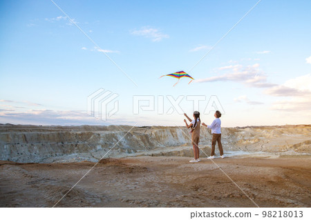 A boy and a girl fly a kite standing on the edge of a high cliff 98218013