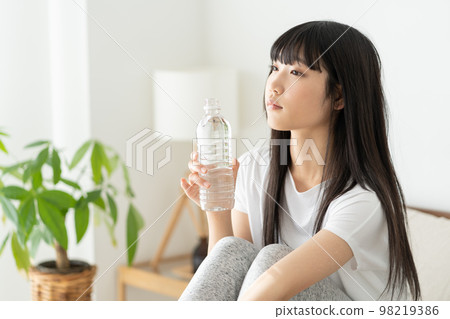 A high school girl holding a plastic bottle of mineral water and staring out the window 98219386