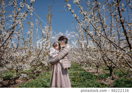 Mother holds child in blooming cherry garden 98222116