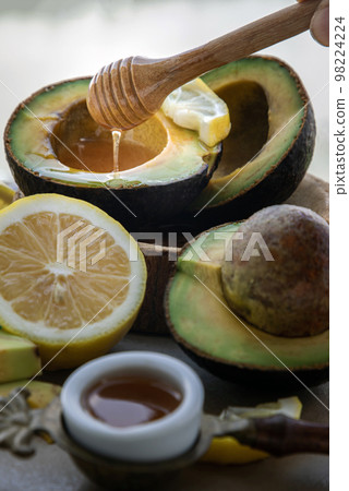 Close-up of Honey dripping from wooden stick dripper into on Fresh organic avocado sliced in half and lemon sliced with honey. 98224224