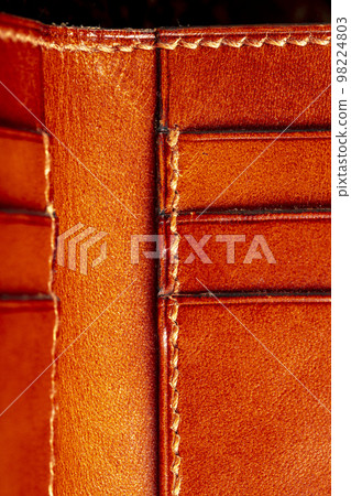 Part of a brown leather wallet or case with stitching. Part of a brown leather wallet or case with stitching. 98224803