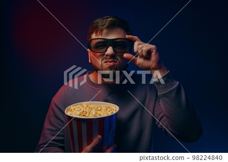 Watching a movie at home. A man watches a movie with a surprised expression on his face. Watching a movie at home. A man watches a movie with a surprised expression on his face. 98224840