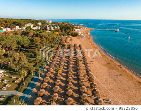 Aerial view of umbrellas, palms on the sandy beach, people, blue sea with waves at sunset. Summer holiday. Tropical landscape with palm trees, parasols, white sand, ocean. Aerial view of umbrellas, palms on the sandy beach, people, blue sea with waves at sunset. Summer holiday. Tropical landscape with palm trees, parasols, white sand, ocean. 98225850