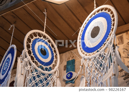 Low angle close-up of dreamcatchers with evil eyes and feathers hanging in a row from roof for sale at shop in Turkish market Low angle close-up of dreamcatchers with evil eyes and feathers hanging in a row from roof for sale at shop in Turkish market 98226167