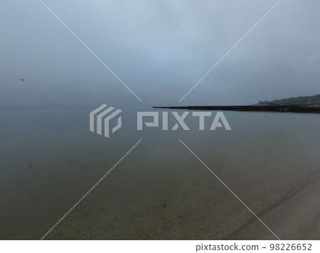 Sandy beach on calm sea. Calm sea cloudy weather. Smooth waveless sea surface in windless cloudy weather. Calmness. Rainy weather. Pure transparent water. Shoreline coast sea line. Natural background Sandy beach on calm sea. Calm sea cloudy weather. Smooth waveless sea surface in windless cloudy weather. Calmness. Rainy weather. Pure transparent water. Shoreline coast sea line. Natural background 98226652