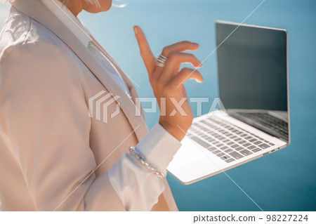 Freelance close up woman hands writing on computer. Well looking middle aged woman typing on laptop keyboard outdoors with beautiful sea view. Freelance close up woman hands writing on computer. Well looking middle aged woman typing on laptop keyboard outdoors with beautiful sea view. 98227224