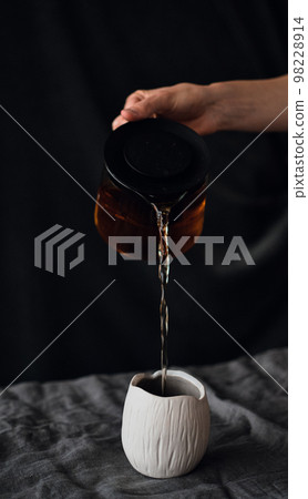 pouring tea from a teapot into an earthenware mug pouring tea from a teapot into an earthenware mug 98228914