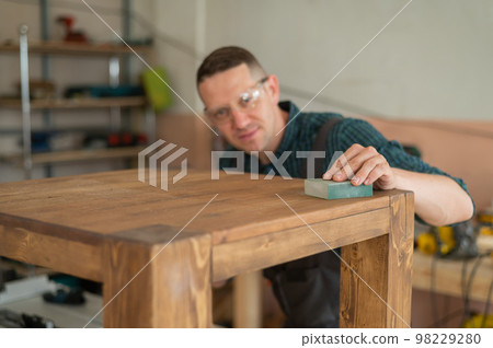 Male carpenter finishing work on wooden table in workshop.  98229280
