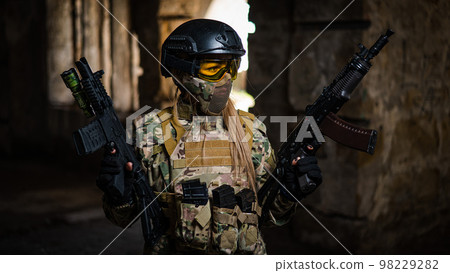 A woman in an army uniform holds a firearm in an abandoned building. 98229282