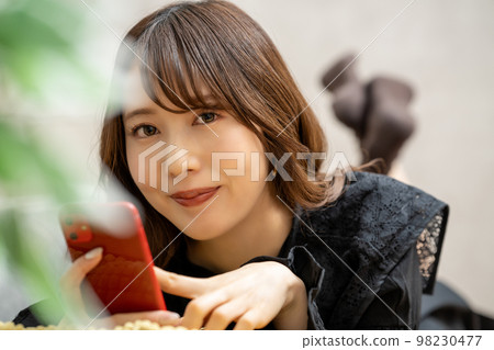 A young woman lying down and using a smartphone A young woman lying down and using a smartphone 98230477
