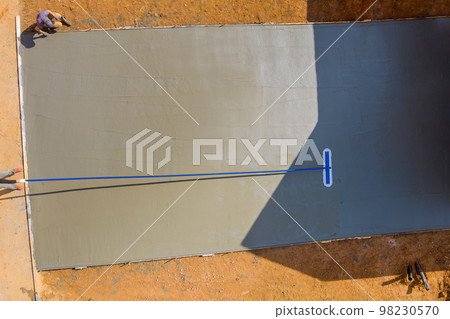 This worker holding steel fresno trowel and smoothing out new sidewalk on newly poured sidewalk, which is still wet. 98230570