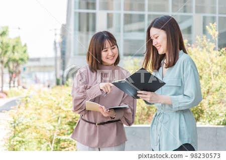 A smiling Asian college student and business woman studying while looking at a notebook in front of a building A smiling Asian college student and business woman studying while looking at a notebook in front of a building 98230573