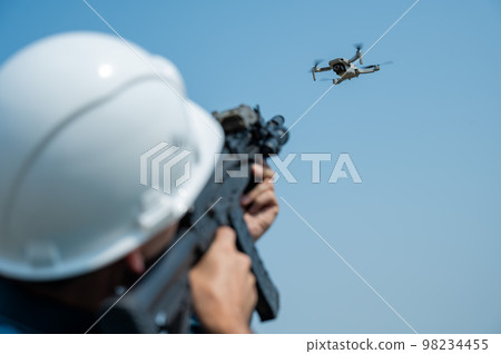 Caucasian man in a helmet shoots a flying drone with a rifle. Caucasian man in a helmet shoots a flying drone with a rifle. 98234455