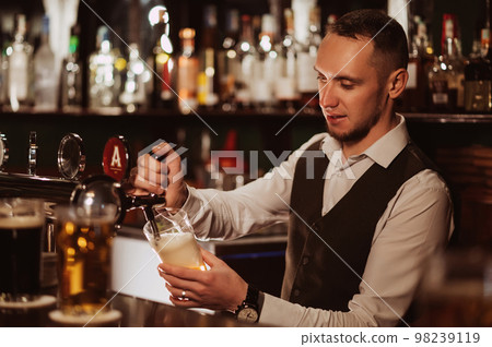 bartender pours draft beer into a glass from the tap behind the bar counter bartender pours draft beer into a glass from the tap behind the bar counter 98239119