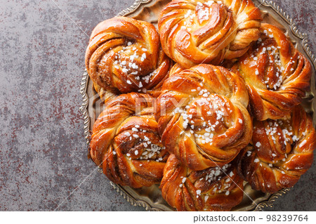 Kanelbullar or Kanelbulle is a traditional Swedish cinnamon buns flavored with cinnamon and cardamom spices and topped with pearl sugar close-up on a plate. Horizontal top view 98239764