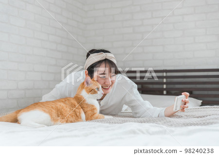 與寵物貓玩耍的亞洲女性在家裡的臥室裡用智能手機拍照 98240238