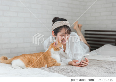 與寵物貓玩耍的亞洲女性在家裡的臥室裡用智能手機拍照 與寵物貓玩耍的亞洲女性在家裡的臥室裡用智能手機拍照 98240240