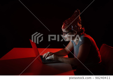 Paranoid caucasian woman typing on a computer wearing a tinfoil cap. Conspiracy theory. Paranoid caucasian woman typing on a computer wearing a tinfoil cap. Conspiracy theory. 98240411