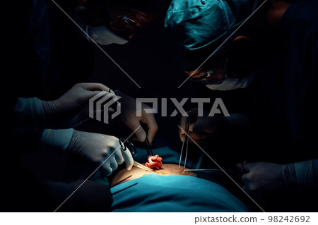 Surgical team performing surgery to patient in sterile operating room. Surgical team performing surgery to patient in sterile operating room. 98242692