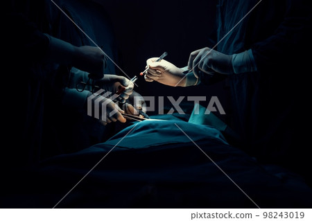 Closeup surgical team performing surgery to patient in sterile operating room. 98243019
