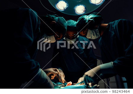 Surgical team performing surgery to patient in sterile operating room. Surgical team performing surgery to patient in sterile operating room. 98243464