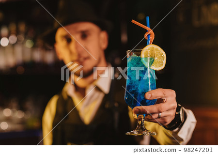 bartender serves a cocktail Blue Lagoon in a glass with a straw at bar counter bartender serves a cocktail Blue Lagoon in a glass with a straw at bar counter 98247201