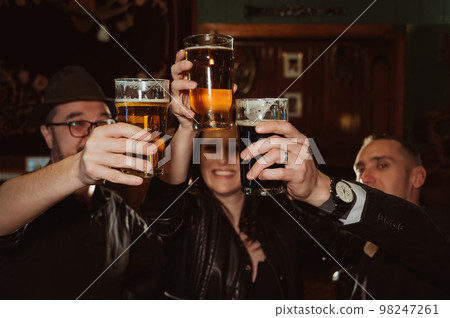 three happy friends happily clink glasses with beer behind bar counter 98247261