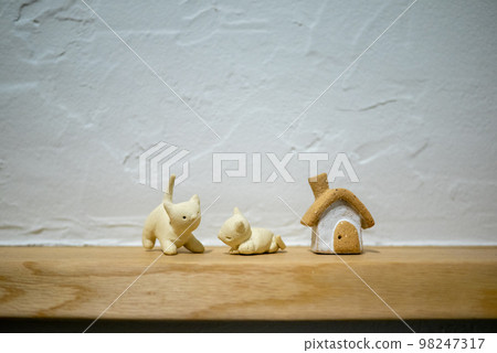 An unglazed pottery house and two cat figurines in front of a diatomaceous earth wall 98247317