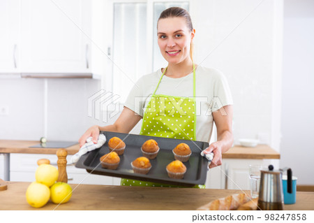 Woman holding sheet pan with just baked cupcakes. Woman baking cakes at home Woman holding sheet pan with just baked cupcakes. Woman baking cakes at home 98247858