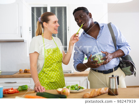 Wife in apron feeding her husband celery at breakfast Wife in apron feeding her husband celery at breakfast 98247919