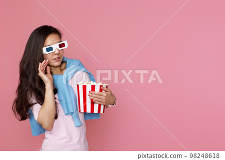 woman watching movie film, holding bucket of popcorn woman watching movie film, holding bucket of popcorn 98248618