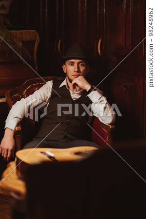 stylish man in hat is sitting in an armchair in a chic retro interior of restaurant stylish man in hat is sitting in an armchair in a chic retro interior of restaurant 98248962