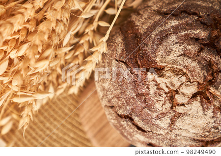 Freshly baked rye bread on a yeast-free starter and on a mixture of whole grain, rye and wheat flour. It lies on a napkin, next to a dried flower with grains. Selective focus. Closeup with copy space. 98249490