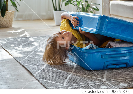 A child sitting in a suitcase have fun and hiding, waiting for a trip on vacation, look at camera A child sitting in a suitcase have fun and hiding, waiting for a trip on vacation, look at camera 98251024