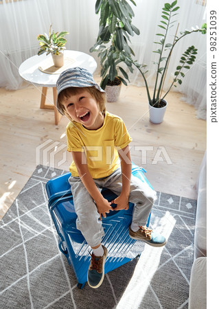 A child sitting on a suitcase have fun and laughs, waiting for a trip on vacation 98251039