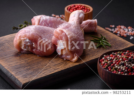 Three raw chicken legs with spices and herbs on a wooden cutting board 98253211
