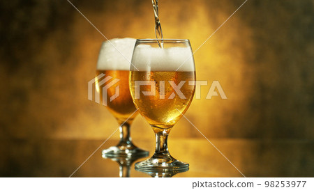 Glass of pouring light beer on dark golden background. 98253977